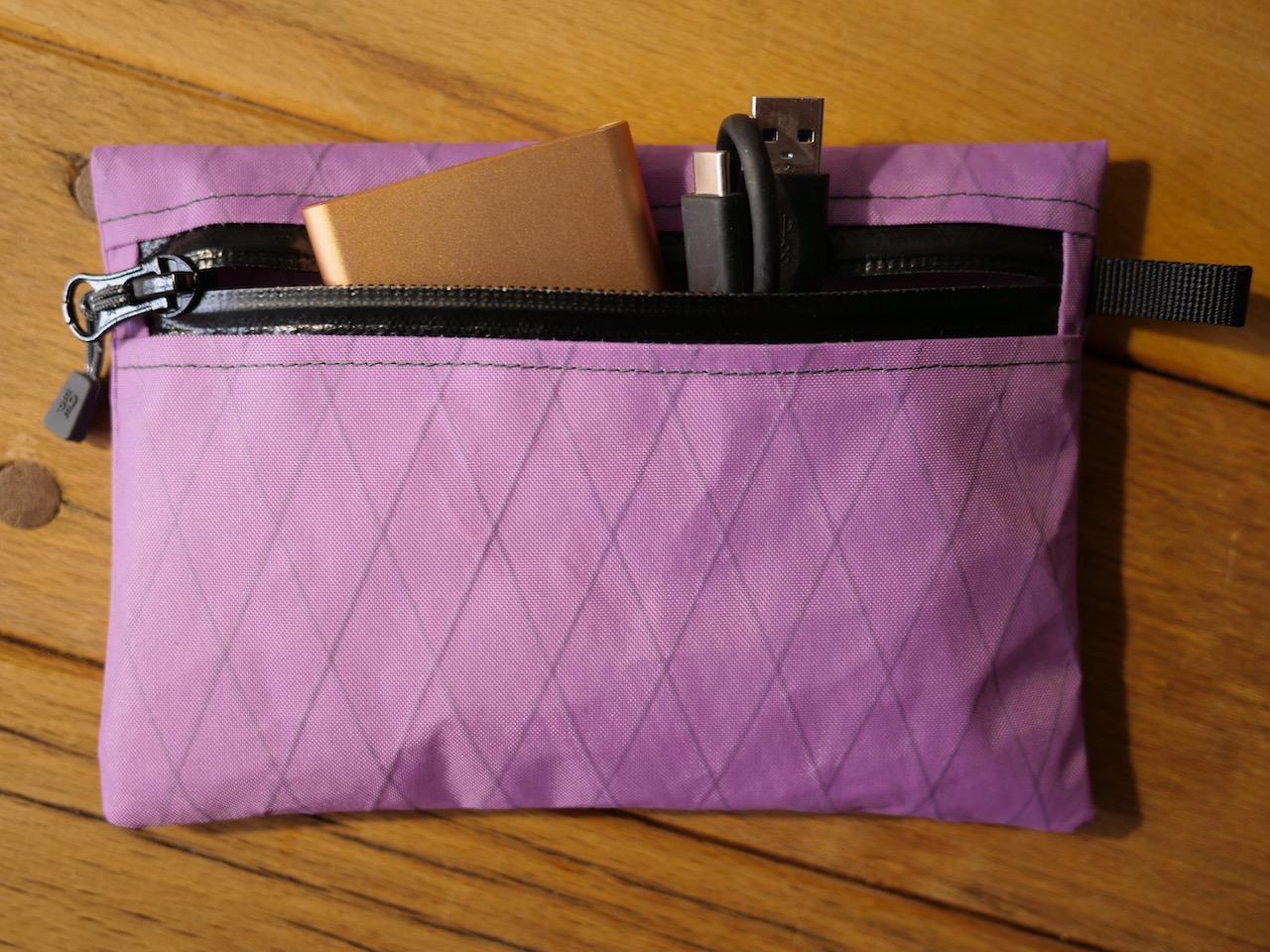 Zipperbag 13×18 von kirschpack in Flieder aus X-Pac, mit Kabeln und Notizbuch in der Öffnung
